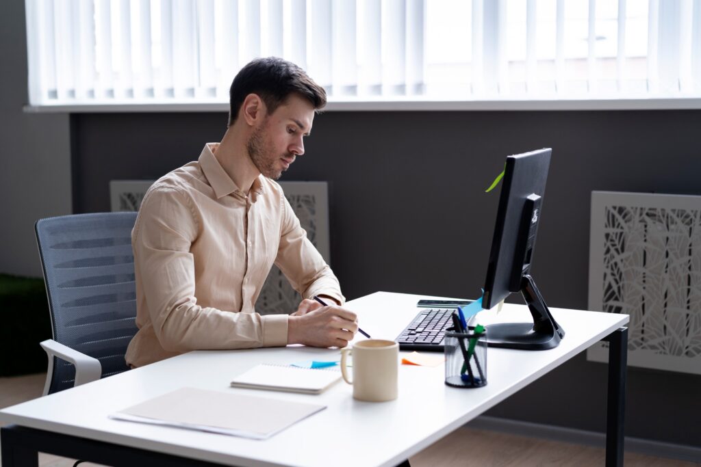 A man at a desk with a computer and pen